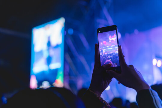Girl holding smart phone and photographing in music festival concert, party event background concept	
