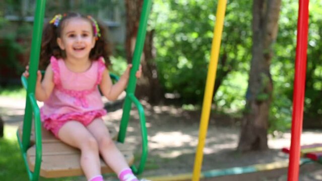 Mother is tickling her pretty curly daughter on swing.