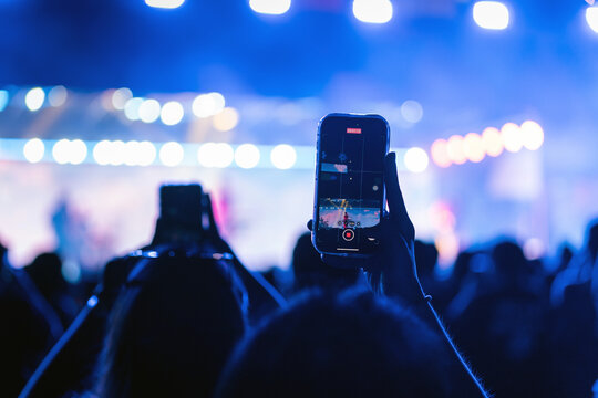 Girl holding smart phone and recording and photographing in music festival concert, party event background concept	
