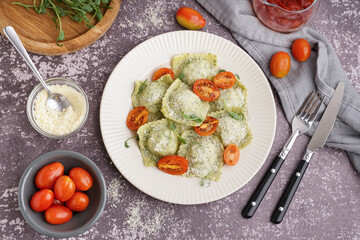 Plate of tasty ravioli with tomatoes and cheese on grey background