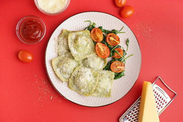 Plate of tasty ravioli with tomatoes and cheese on red background