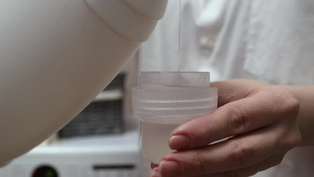 woman pouring laundry detergent into measuring cup, close up