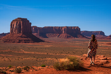 Woman in a pretty dress overlooking Monument Valley, Utah, USA, on a clear sunny day in spring, standing at Artist's point. Blue sky, long shadows.