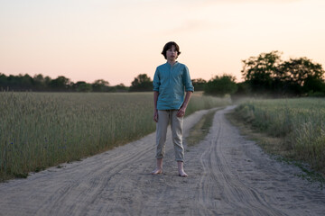 Obraz premium A barefoot teenager in comfortable clothes stands on a dirt road.