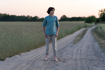 A barefoot teenager in comfortable clothes stands on a dirt road.