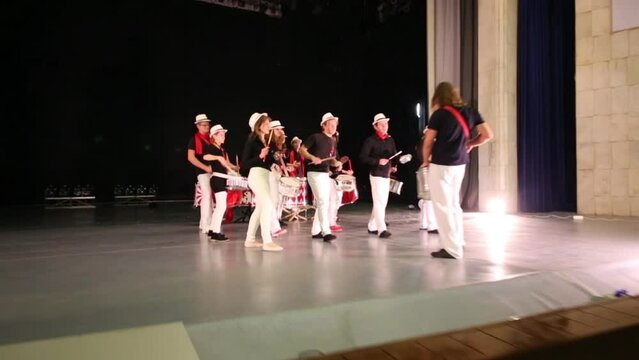 Musical group of fourteen people in hats play drums