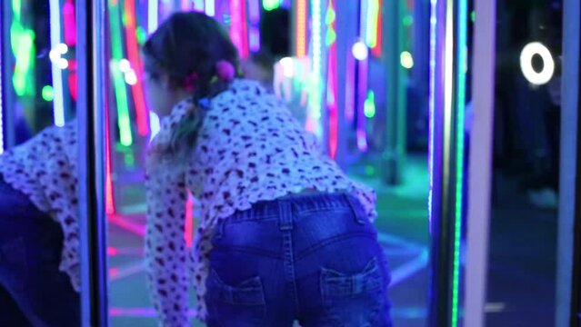Little girl walks on all fours in mirror labyrinth illuminated