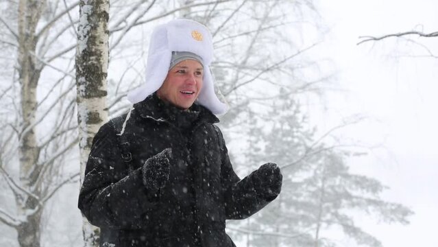 A man in hat with earflaps standing in the forest under snow