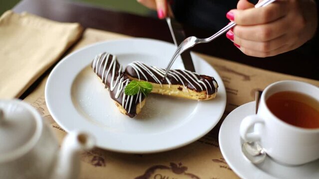 Female hands cut choux pastry apart by fork and knife 