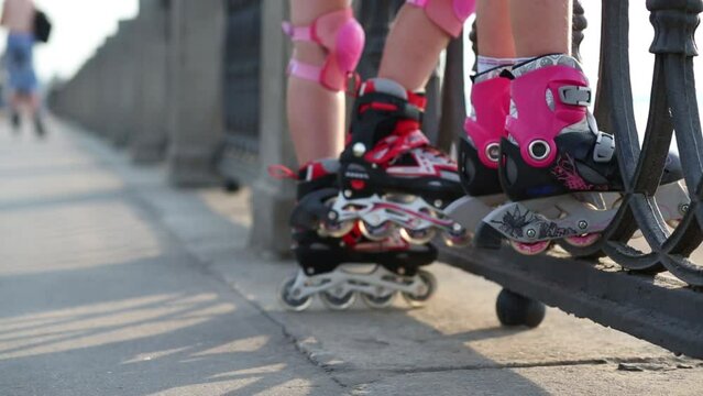Legs of little girls in roller skates standing near railing 