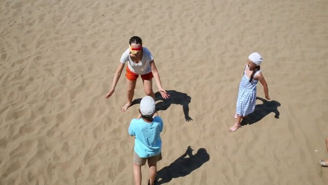 Mother with three children play blindman buff on yellow sand