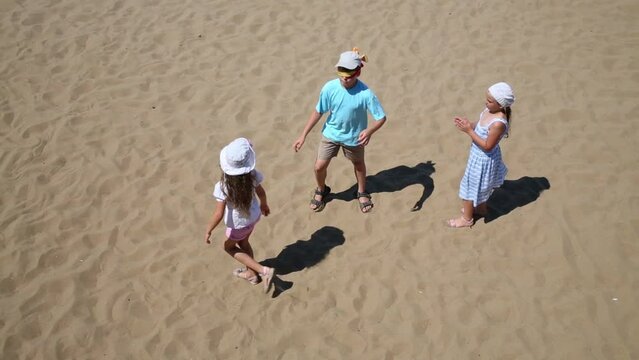 Three happy children play blindman buff on yellow sand of beach