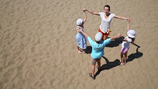 Woman with three children round dance on yellow sand of beach
