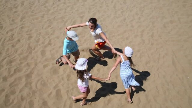 Woman with children run around in circle holding hands on sand 