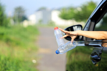 female driver's hand throwing plastic bottle trash through the car window. bad habits that damage the environment and are sources of environmental pollution
