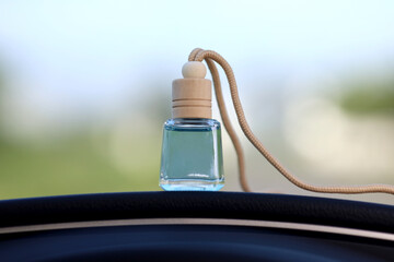 Blue car air freshener with glass bottle packaging and wooden cover on car dashboard with outdoor...