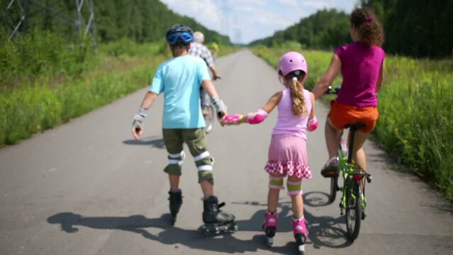 Back of boy and girl roller-skate and mother rides bike on road