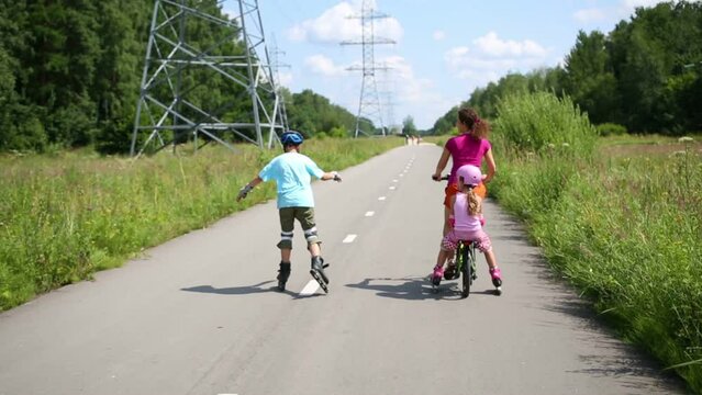 Back of boy roller-skating and mother riding bike with girl 