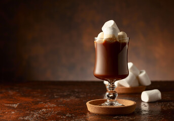 Hot chocolate with marshmallows in a glass mug on a old brown table.