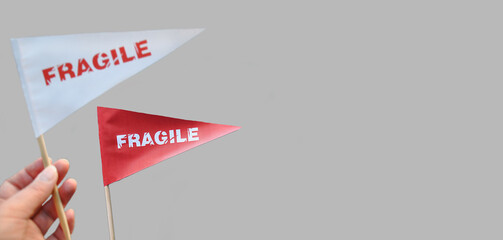 Small paper flags in hand with the warning 'Fragile' as a label. The concept of fragile products. Monochrome background. Copy space