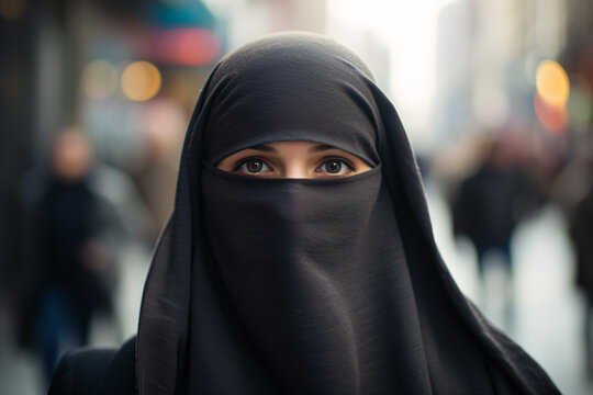 Young woman covered with Muslim Niqab face veil with only eyes visible with blurry city street in background
