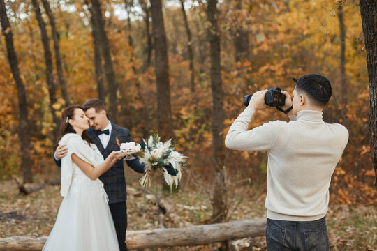 male wedding photographer taking pictures of the bride and groom in nature in autumn