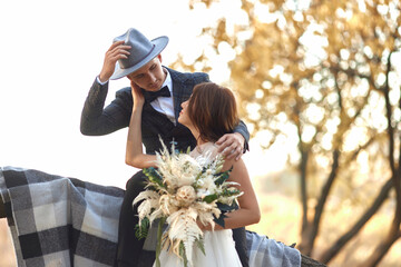 beautiful happy stylish bride and groom in hat near tree in autumn