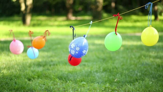 Many colorful balloons hang on clothesline on wind at summer park