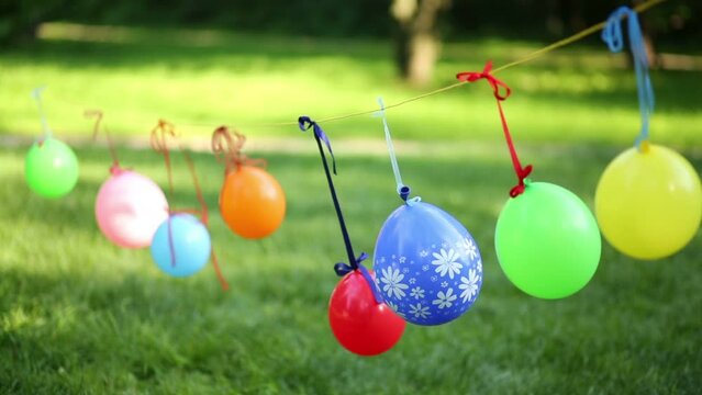 Many children balloons hang on clothesline on wind at summer park