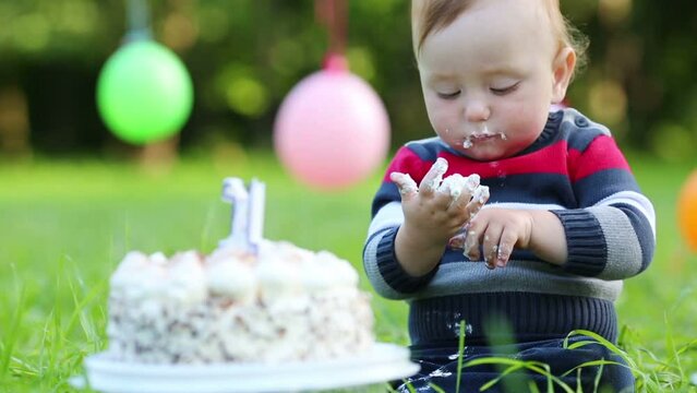 Cute stained happy baby eats cake with candle in form of 1