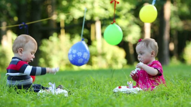 Two stained babies eat cakes with candles in form of 1