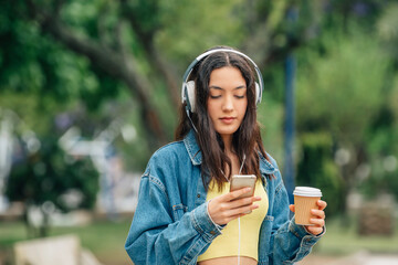 girl on the street looking at mobile phone with headphones and cup of coffee