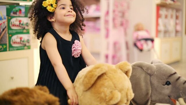 Little cute girl swings on soft toy bear in store with toys