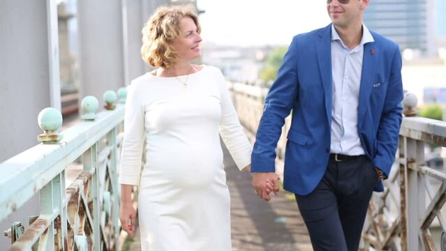 Pregnant woman in white and man walk together on railway bridge