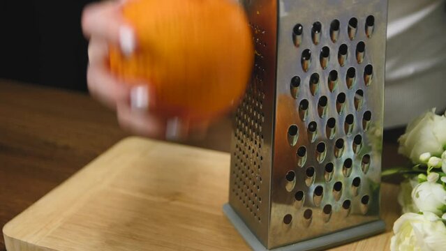 Woman grating orange zest on wooden table in the kitchen