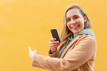 Fototapeta premium Young blonde woman at outdoors using mobile phone and pointing back
