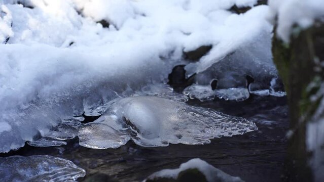 Crystal clear water flowing down a ice and snow covered stream in Laterns, Austria