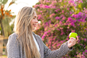 Young blonde woman with an apple at outdoors with happy expression