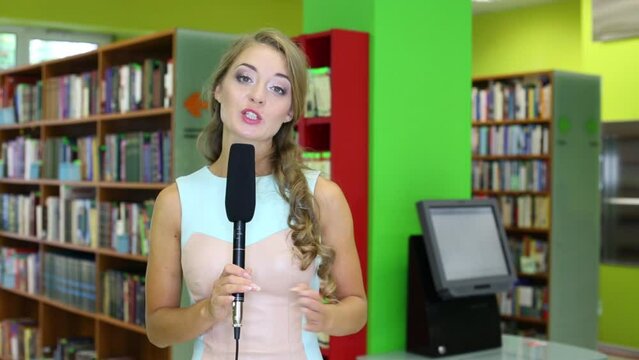 beautiful girl with a microphone in hand next to bookshelves