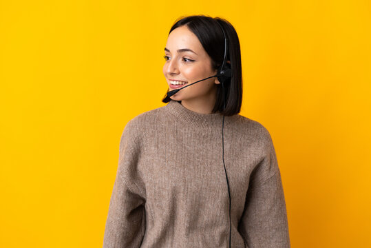Young telemarketer woman isolated on yellow background looking to the side and smiling