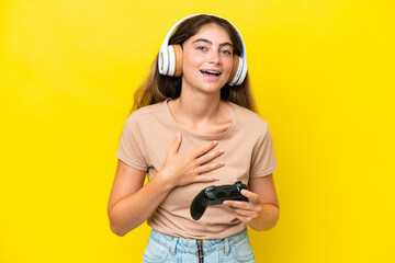 Young caucasian woman playing with a video game controller isolated on yellow background smiling a...