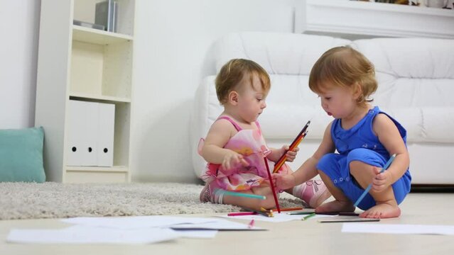 Two little cute girls paint pencils on floor in room at home