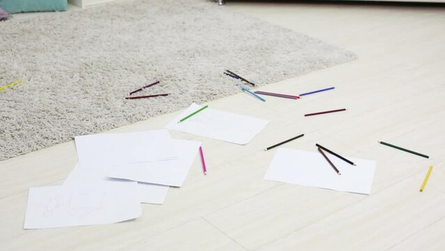 Many pencils and paper sheets with kids draws on floor in room
