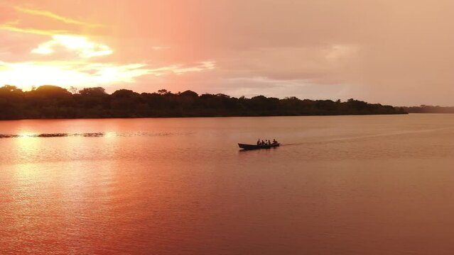 Aerial view of fishing boat with tourists in Amazon river. Amazing beautiful red yellow sunset clouds and sky. Jungle trees background. Vacation time journey with boat trip. 4K wide angle