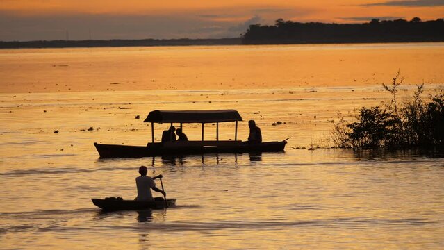 Tourists ride in a traditional boat in the Amazon. A beautiful sunset over the river. Locals take tourists on boat trips. Amazing sunrise sky and clouds, jungle trees background. 4K telezoom footage.