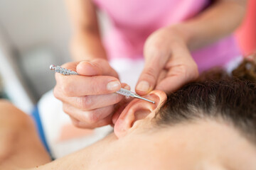 Crop beautician applying flexible massage brass ear pen on female client in salon
