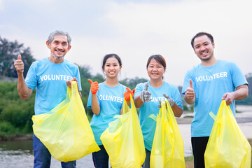 group of family volunteers in blue T-shirt standing,holding yellow plastic sorting bags and doing...