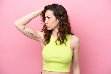 Young caucasian woman isolated on pink background having doubts while scratching head