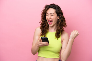 Young caucasian woman isolated on pink background with phone in victory position