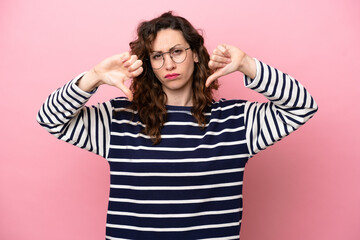 Young caucasian woman isolated on pink background showing thumb down with two hands